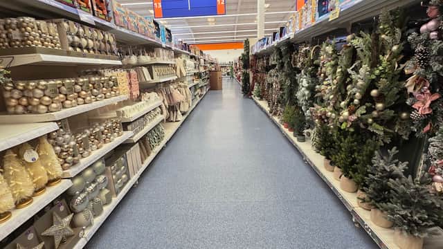 A brightly lit retail aisle filled with festive decorations, including trees, ornaments, and garlands on both sides.