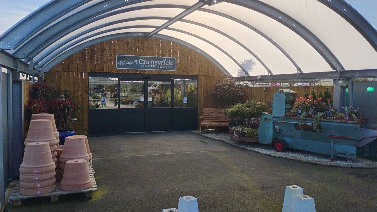 Entrance to Cranswick Garden Centre featuring colorful flower displays and a sign above. Bright blue sky in the background.
