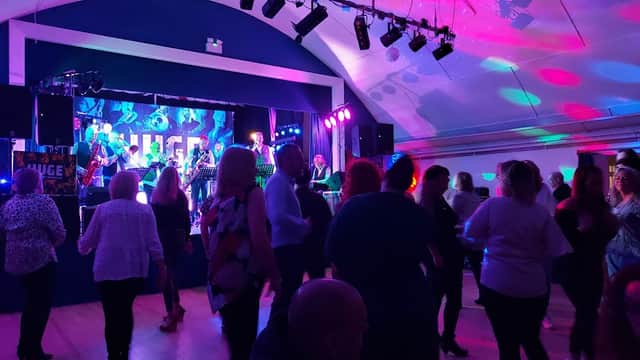 A lively event with people dancing, colorful lights, and a band performing on stage at Stockton on the Forest Village Hall.