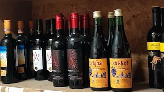 Shelves filled with various bottles of red wine, showcasing different labels and brands in a cozy corner shop.