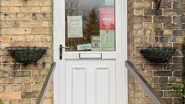 White door with glass panel, "St Catherine's House" sign, and potted plants on either side. Open sign visible.