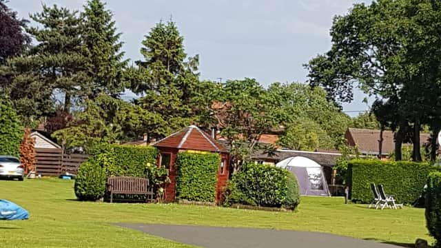 Lush green lawn with a gazebo, benches, and tents, surrounded by trees and a clear blue sky at Pembroke Caravan Park.
