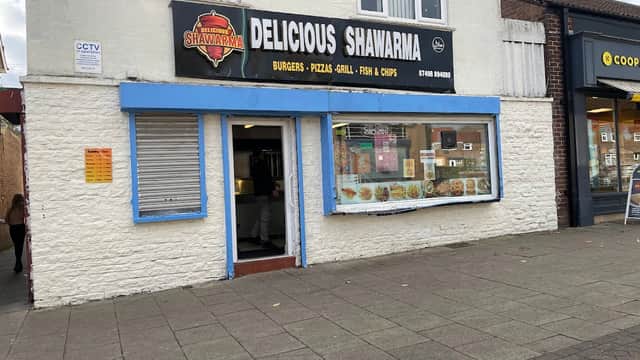 Restaurant exterior with a sign reading "Delicious Shawarma," featuring a menu display and nearby shops in Eastfield.