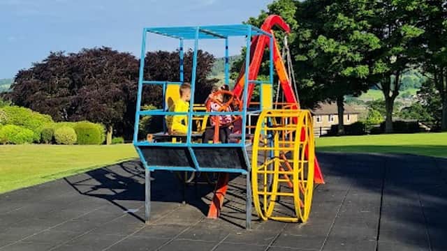 Colorful playground equipment with swings and slides on a grassy area under a blue sky with scattered clouds.
