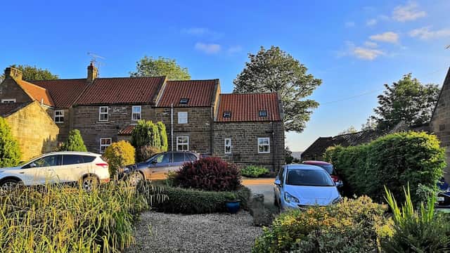 Cottages with red roofs surrounded by greenery and parked cars under a clear blue sky in Fryup, Yorkshire.