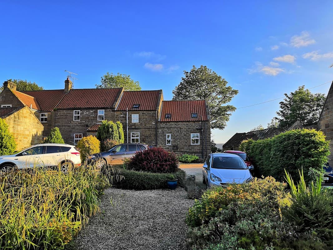 Cottages with red roofs surrounded by greenery and parked cars under a clear blue sky in Fryup, Yorkshire.