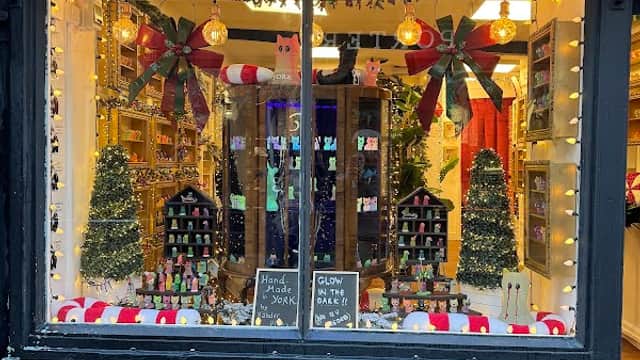 Gift shop window decorated with festive lights, trees, and colorful displays, featuring "CATS" and "GLOW IN THE DARK" signage.