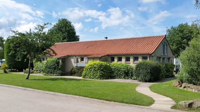 Single-story building with a red-tiled roof, surrounded by greenery and a pathway in Ripley Caravan Park.