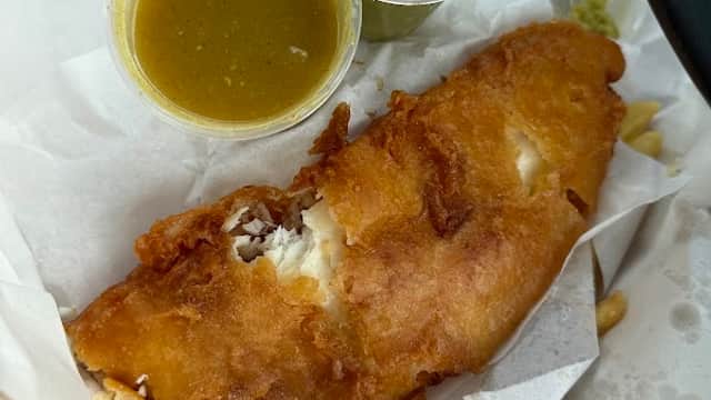 Crispy battered fish fillet with two sauces in cups, served on white paper.