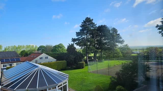 Burythorpe House features a conservatory, lush green lawn, tennis court, and trees under a clear blue sky.