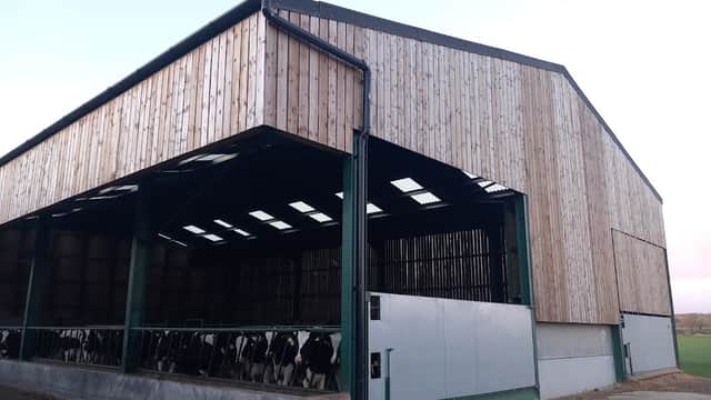 Large wooden barn with open sides, housing cows, set in a rural landscape in Great Edstone, Yorkshire.