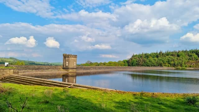 A serene landscape featuring a reservoir with a stone tower, surrounded by lush greenery and blue sky with clouds.