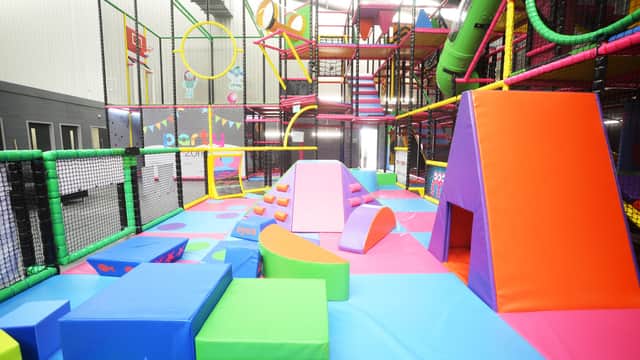 Vibrant indoor play area with colorful climbing structures, slides, and padded obstacles under a high ceiling.