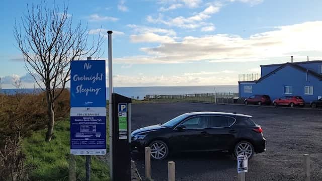 Pay & Display car park at Reighton Sands, featuring a parked car, sign, and a view of the sea in the background.
