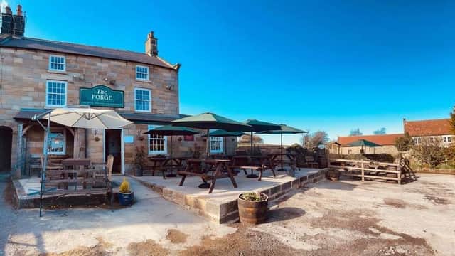 The Forge Inn features outdoor seating with umbrellas, stone exterior, and a clear blue sky in Aislaby, Yorkshire.