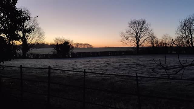 Frosty field at dawn, with bare trees and a fence outlining the landscape under a colorful sky.