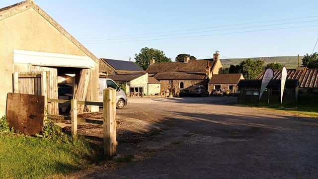 A rustic caravan site with stone buildings, parked vehicles, and green fields under a clear blue sky in Redmire, Yorkshire.