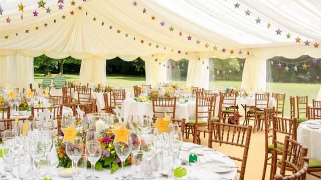 Elegant marquee decorated with colorful stars, featuring round tables set with floral centerpieces and glassware.