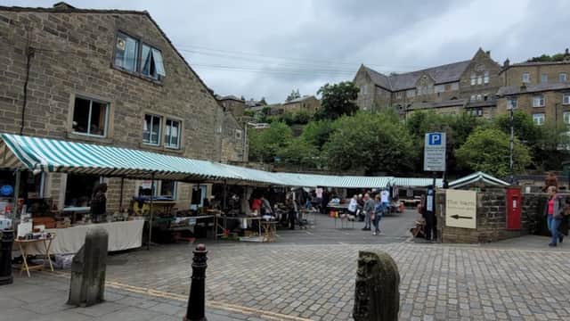 Market stalls with striped canopies line a cobblestone street, surrounded by stone buildings and greenery in Chiserley.