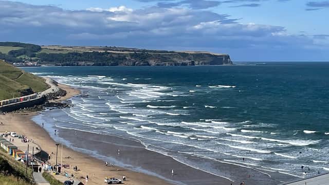 North Terrace Car Park overlooking a sandy beach with waves, colorful beach huts, and cliffs in the background.