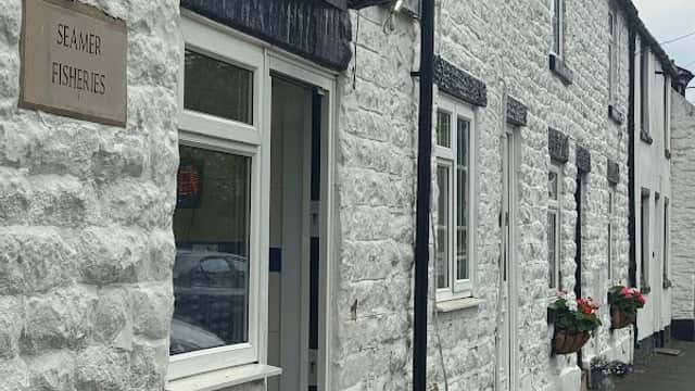White stone building with a sign reading "Seamer Fisheries" and flower boxes under the windows. Litter bins nearby.