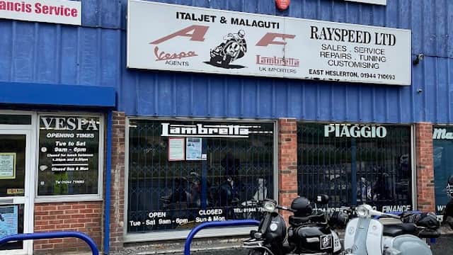Blue shopfront with signs for Lambretta, Vespa, and Rayspeed Ltd; scooters displayed in the window.