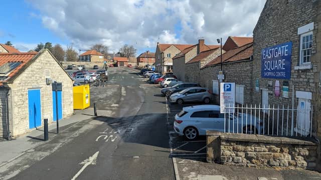 Eastgate Car Park with cars parked, stone buildings, blue sky, and clouds, near Eastgate Square Shopping Centre.