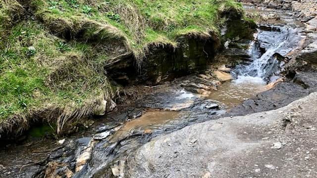 A small stream flows through rocky terrain with grassy banks in a scenic landscape of Westerdale, Yorkshire.