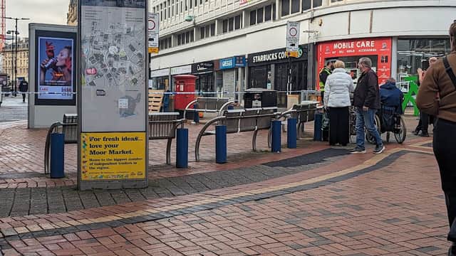 Shopping area with a map display, benches, people walking, and nearby storefronts in Sheffield, Yorkshire.