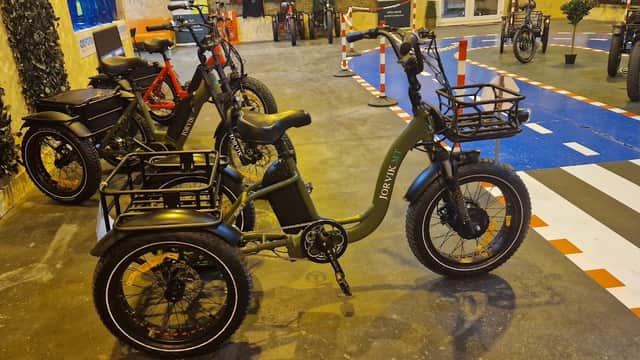 A green Jorvik tricycle with baskets, surrounded by various bikes in a sports shop setting.