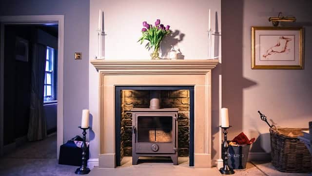 A cozy living room featuring a stone fireplace, a wood stove, candles, and a vase of tulips on the mantel.