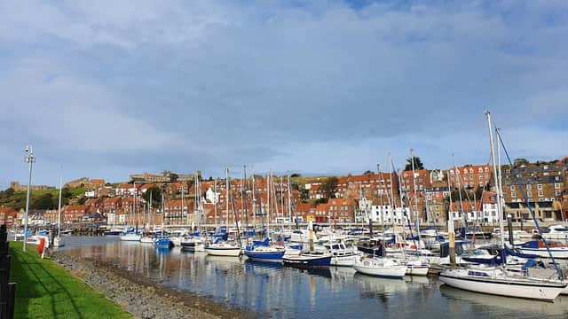 Harbor with moored sailboats, colorful buildings on the hillside, and a cloudy blue sky in Whitby, Yorkshire.