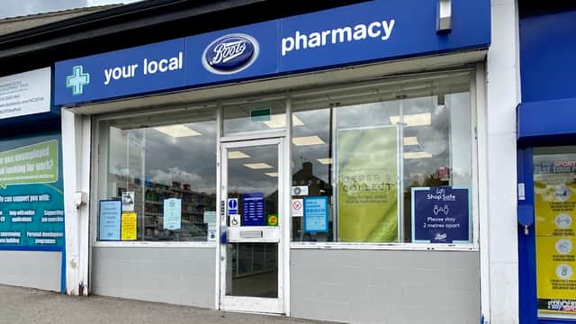 Boots Pharmacy storefront with blue signage, large windows, and various posters displayed outside.