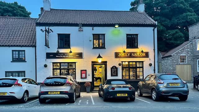 The Jolly Sailor Inn with a white exterior, warm lights, and parked cars in front, set in a quaint Yorkshire village.