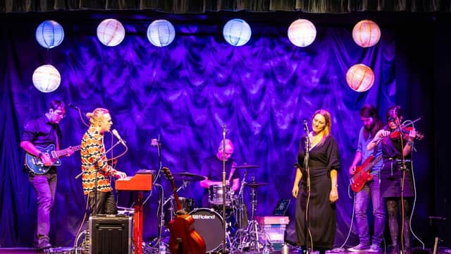 A lively performance on stage with musicians, instruments, and colorful lanterns against a purple backdrop.