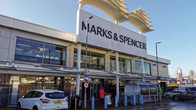 M&S Simply Food storefront with large signage, outdoor seating, and a parked car in front on a sunny day.