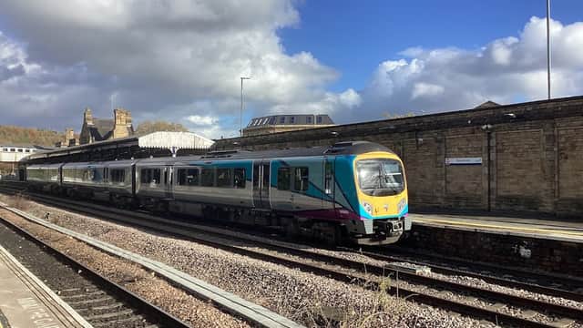 A train at Dewsbury Railway Station, with stone buildings and a blue sky in the background.