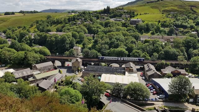 A scenic view of Walsden, Yorkshire, featuring green hills, a railway bridge, and quaint buildings nestled among trees.