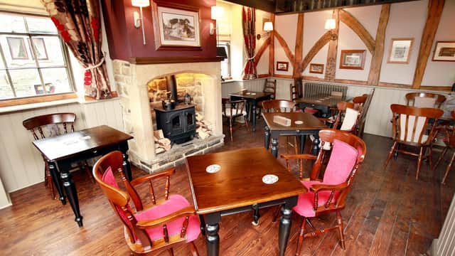 Cozy bar interior with wooden tables, chairs, a stone fireplace, and framed pictures on the walls.