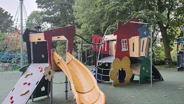 Colorful playground equipment with a slide, climbing structures, and surrounding trees in Bramhope, Yorkshire.