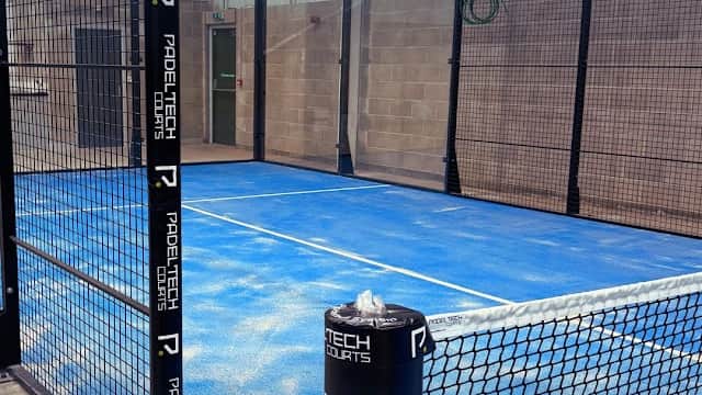 Indoor padel court with blue flooring, surrounded by black mesh fencing, featuring branding for ProTech Sports.