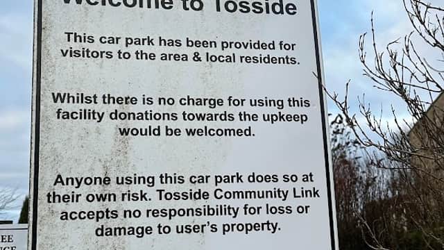 Welcome to Tosside sign detailing car park usage, charges, and liability information, with a blue no overnight parking sign below.