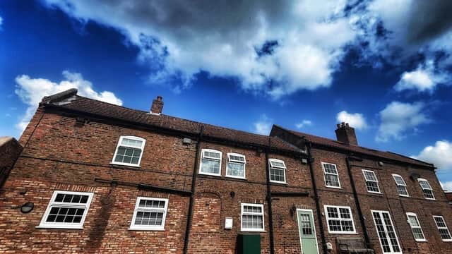 Red-brick guest house with multiple windows, green door, and a bench under a dramatic sky in Cawood, Yorkshire.