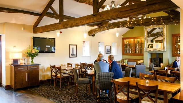 Cozy bar interior with wooden beams, tables, chairs, and a TV; patrons enjoying drinks in a warm atmosphere.