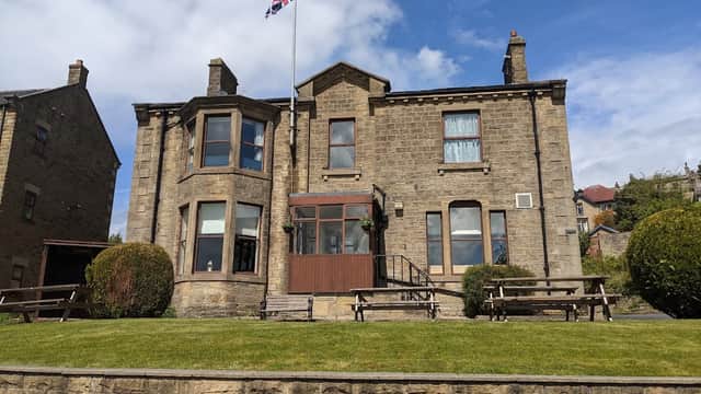 Historic stone building with a Union Jack flag, surrounded by green lawn and benches, in Riddlesden, Yorkshire.