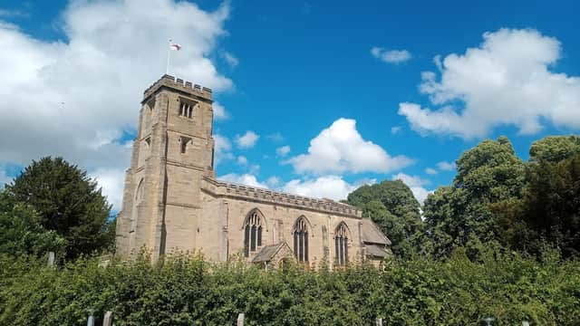 Historic stone church with a tall tower, surrounded by lush greenery and a bright blue sky with fluffy clouds.