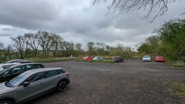 Gravel car park with several parked cars surrounded by trees and overcast skies in Huggate, Yorkshire.