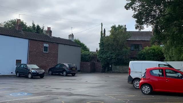 Free parking area with several cars, surrounded by brick buildings and trees under a cloudy sky.