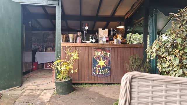 Wooden bar with "The Star Inn" sign, plants in pots, and a cozy outdoor seating area in a rustic setting.