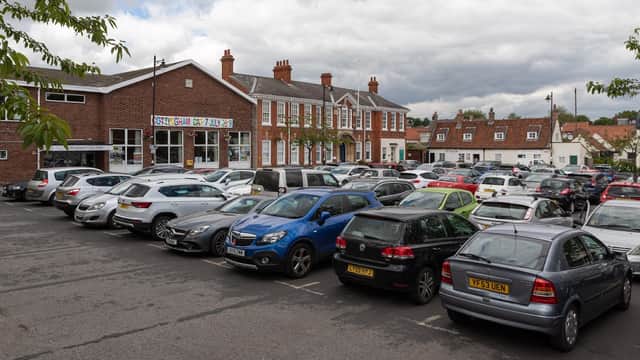 Busy Cottingham Green Car Park filled with parked cars, adjacent to a brick building and residential homes under a cloudy sky.
